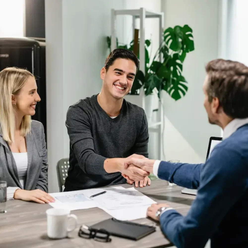 young-happy-couple-making-agreement-with-their-financial-advisor-home-men-are-shaking-hands