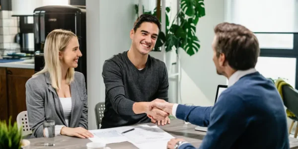 young-happy-couple-making-agreement-with-their-financial-advisor-home-men-are-shaking-hands