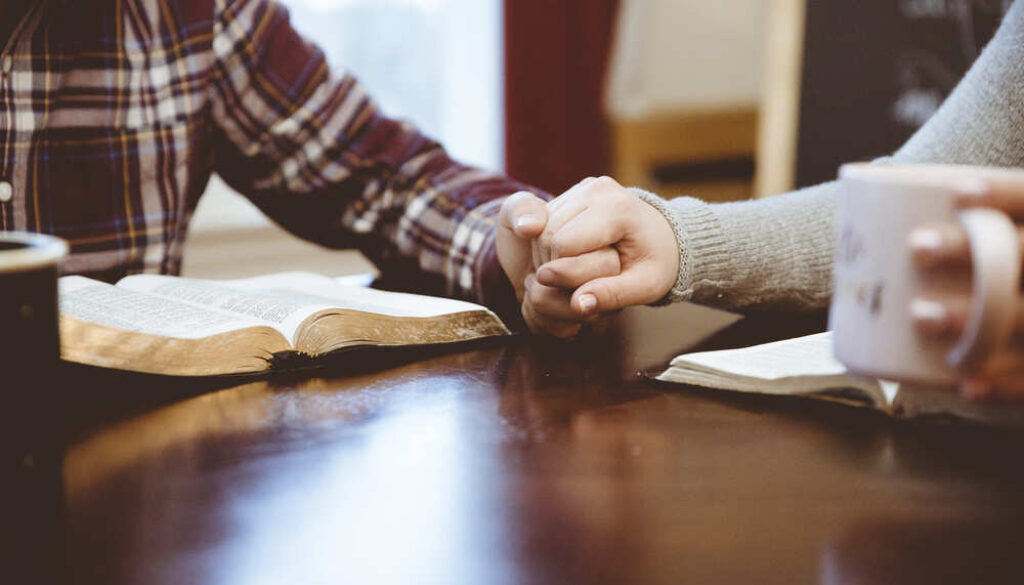 closeup-shot-couple-holding-hands-table-white-reading-their-books (1)
